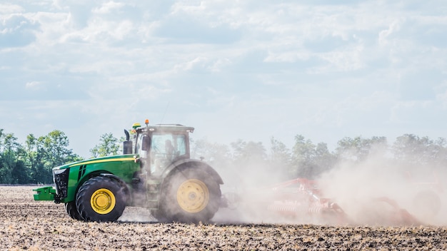 Un tractor verde está trabajando en el campo. Cultivo del suelo. Trabajo agrícola.