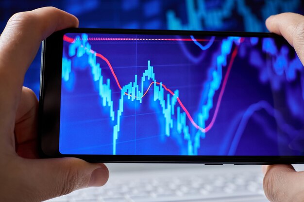 Trader analisa dados do mercado de ações em smartphone no fundo de gráficos de ações