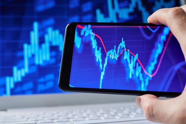 Trader analysiert Börsendaten im Smartphone vor dem Hintergrund von Aktiencharts