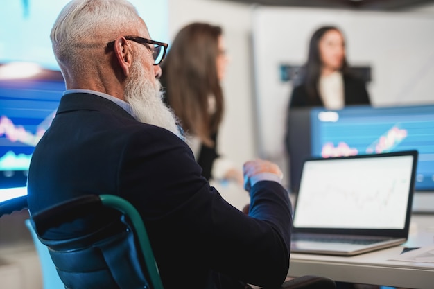 Trader-Team, das eine Börsenanalysekonferenz im Hedgefonds-Büro abhält - Konzentrieren Sie sich auf das Gesicht eines älteren Mannes, der im Rollstuhl sitzt