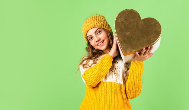 Tradição do dia dos namorados. Seja meu namorado. Boas férias de inverno. Menina alegre de malha chapéu e camisola. Criança segurar fundo de caixa verde de presente de coração. Idéia de celebração do dia dos namorados. Humor romântico.