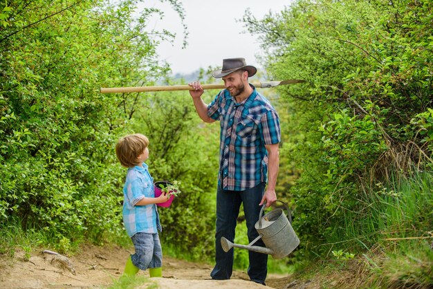 Tradición de plantación de árboles Pequeño ayudante en el jardín Plantando flores Cultivando plantas Niño y padre en la naturaleza con regadera y pala Papá enseñando plantas a cuidar a su hijo Día del árbol Plantando árboles