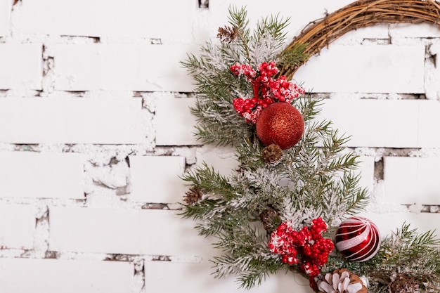 Una tradicional corona de Navidad brillante que cuelga sobre la chimenea en una pared de ladrillo blanco.Concepto de Navidad decoración de año nuevo en estilo loft.