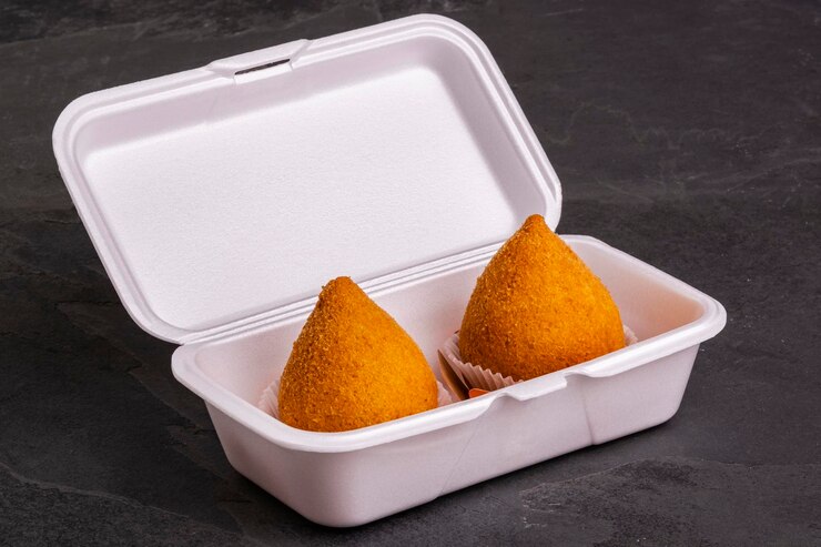 Foto tradicional coxinha frita em embalagem descartável sobre mesa de ardósia.