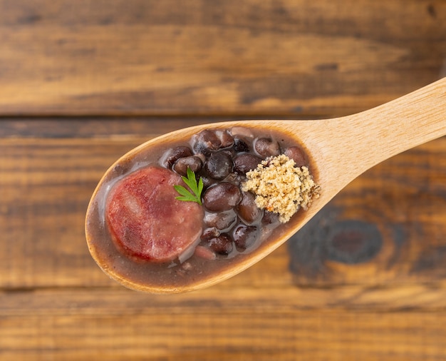 Tradicional feijoada brasileira em uma colher sobre fundo de madeira desfocado.