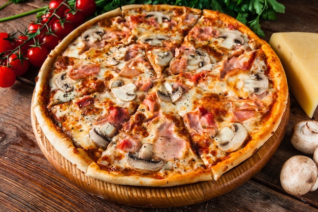 Tradicional pizza italiana com presunto e cogumelos, servida em mesa de madeira rústica decorada com cerejas, queijo, cogumelos, salsa e pimenta em grão. Foto do menu.