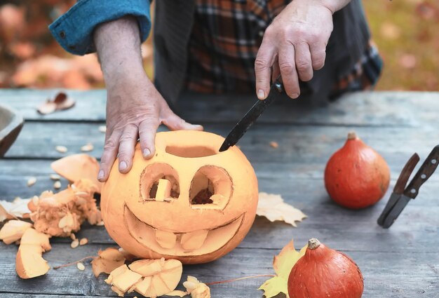 Tradiciones de otoño y preparativos para la fiesta de Halloween. Una casa en la naturaleza, una lámpara hecha de calabazas se corta en la mesa.