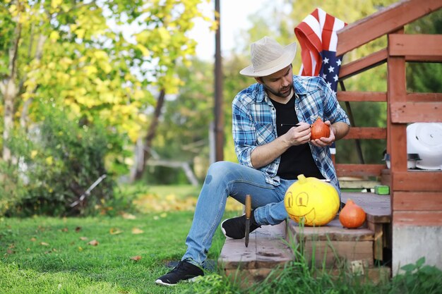 Tradições de outono e preparativos para o feriado de Halloween. Uma casa na natureza, uma lâmpada feita de abóboras está sendo cortada à mesa.