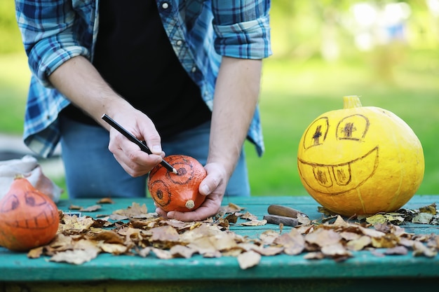 Tradições de outono e preparativos para o feriado de halloween. uma casa na natureza, uma lâmpada feita de abóboras está sendo cortada à mesa.