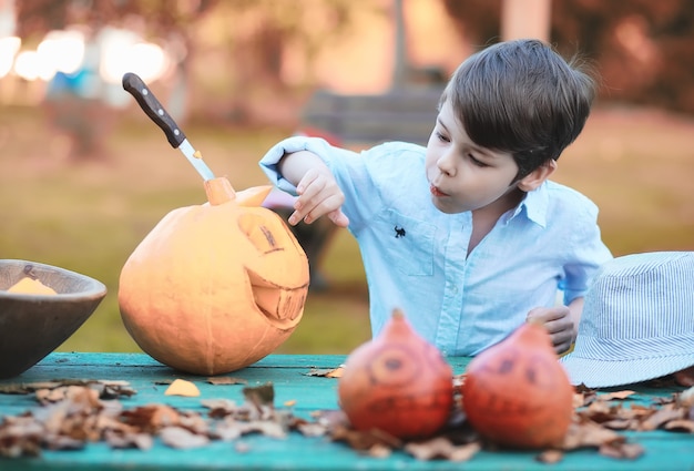 Tradições de outono e preparativos para o feriado de Halloween. Uma casa na natureza, uma lâmpada feita de abóboras está sendo cortada à mesa.