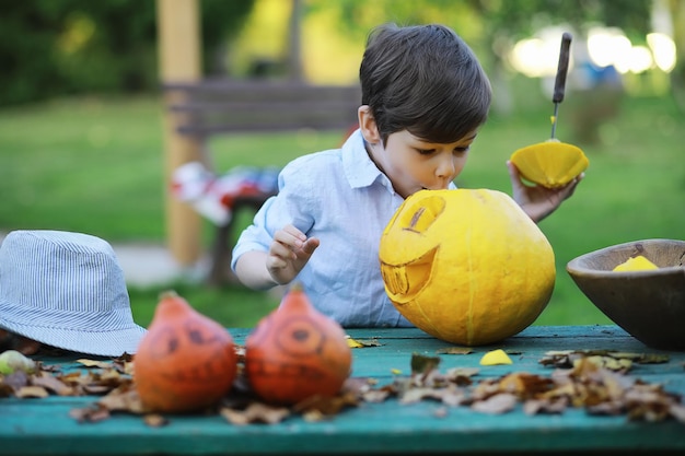 Tradições de outono e preparativos para o feriado de Halloween. Uma casa na natureza, uma lâmpada feita de abóboras está sendo cortada à mesa.