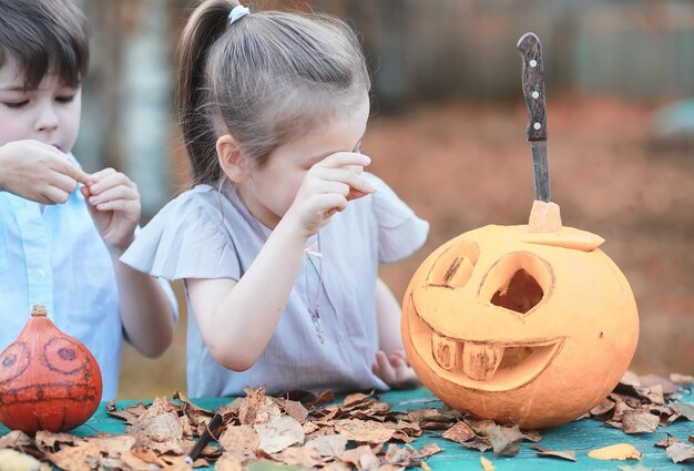 Tradições de outono e preparativos para o feriado de Halloween. Uma casa na natureza, uma lâmpada feita de abóboras está sendo cortada à mesa.