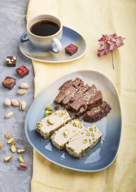 Traditionelle arabische Süßigkeiten Sesam Halva mit Schokolade und Pistazien und eine Tasse Kaffee auf grauem Betonhintergrund Seitenansicht aus nächster Nähe