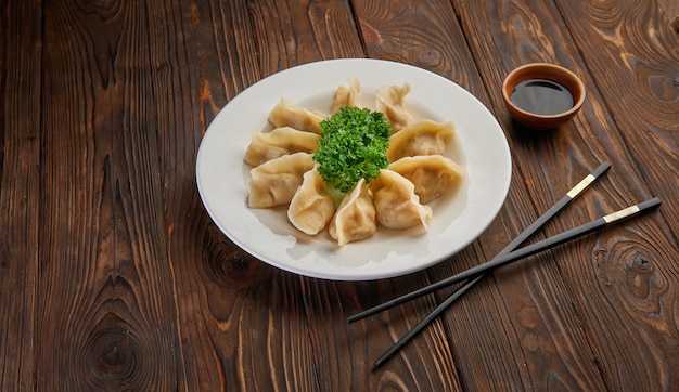 Traditionelle asiatische gebratene Knödel Gyoza auf weißem Teller und Sojasauce mit Paar Essstäbchen auf dunkler Holztischplatte und Kopierraum