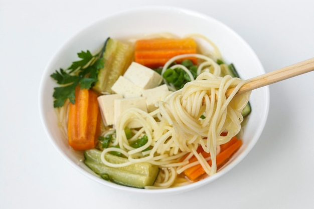 Traditionelle asiatische Suppe mit Tofu-Käse, Nudeln, Karotten und Zucchini auf weißem Hintergrund, Gericht enthält normalerweise Bouillon und Gemüse, horizontale Ausrichtung, Nahaufnahme
