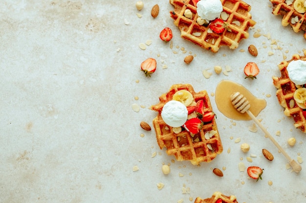 Traditionelle belgische Waffel mit Eis, Erdbeere, Banane, Nüssen und Honig. Sommerliches Frühstück