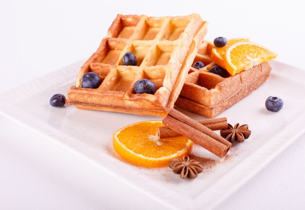 Traditionelle belgische Waffeln mit Blaubeeren, Banane und Zimt auf einer weißen Platte. Gourmet-Frühstück. Nahansicht