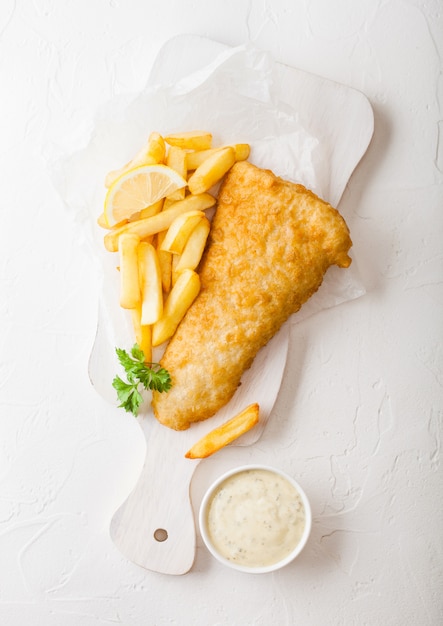 Traditionelle britische Fish and Chips mit Sauce Tartar auf Schneidebrett auf weißem Tisch.