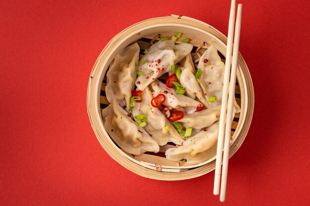 Traditionelle chinesische gedämpfte Teigtaschen im Bambusdampfer mit Holzstäbchen auf rotem Hintergrund, Nahaufnahme, Ansicht von oben. Asiatischer Dim Sum Snack oder Mittagessen