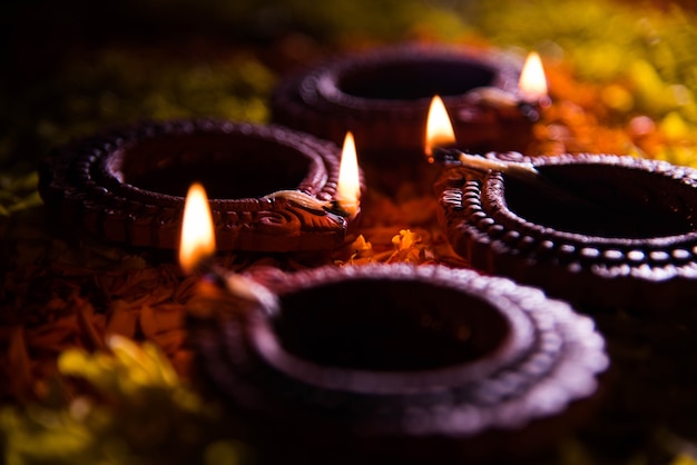 Traditionelle Diya- oder Öllampe, die auf bunten Rangoli aus Blütenblättern beleuchtet ist, auf dem Lichterfest namens Diwali oder Deepawali, selektiver Fokus