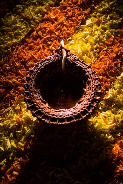 Traditionelle Diya- oder Öllampe, die auf bunten Rangoli aus Blütenblättern beleuchtet ist, auf dem Lichterfest namens Diwali oder Deepawali, selektiver Fokus