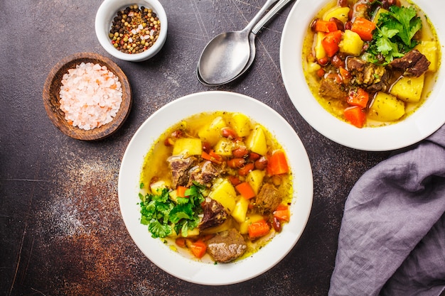 Traditionelle Eintopfsuppe mit Fleisch, Bohnen und Gemüse in einer weißen Platte.