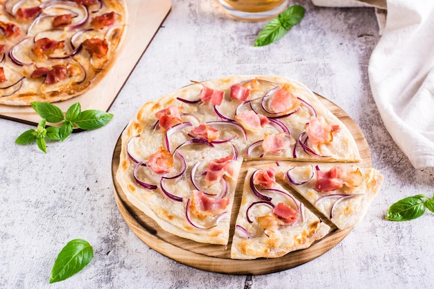 Traditionelle französische Flammkuchen mit Frischkäsespeck und Zwiebeln auf einem Brett auf dem Tisch