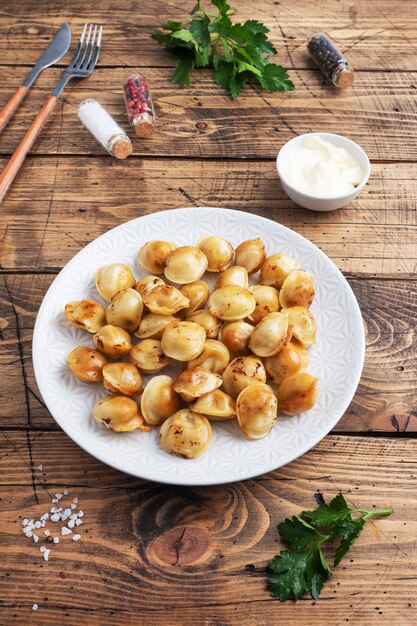 Traditionelle gebratene Pelmeni, Ravioli, Knödel gefüllt mit Fleisch auf Teller, russische Küche. Rustikaler Holztisch, Kopierraum.