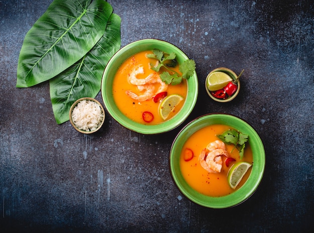 Traditionelle gesunde thailändische Suppe Tom Yum mit Garnelen, Limette, Koriander in Schüssel auf rustikalem Hintergrund mit weißem Reis, Overhead-Schuss. Authentisches Thai-Food-Konzept food