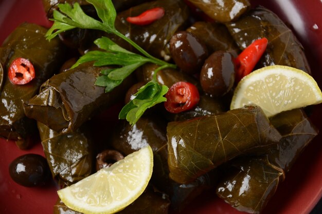 Traditionelle griechische Küche. Eingewickelter Reis in Weinblättern. Dolma mit Zitrone, Gewürzen, verschiedenen eingelegten Oliven und Peperoni.