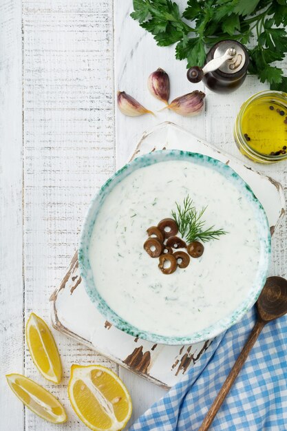 Traditionelle griechische Sauce Tzatziki. Joghurt, Gurke, Dill, Knoblauch und Salzöl in einer Keramikschale auf einer hellen Holzoberfläche