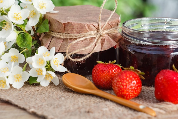 Traditionelle hausgemachte Erdbeermarmelade in Gläsern mit frischen Erdbeeren und Jasmin auf Holztisch