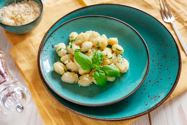 Traditionelle hausgemachte gekochte italienische Kartoffelgnocchi mit Butterpetersilie und Parmesankäse auf weißem Holzhintergrund