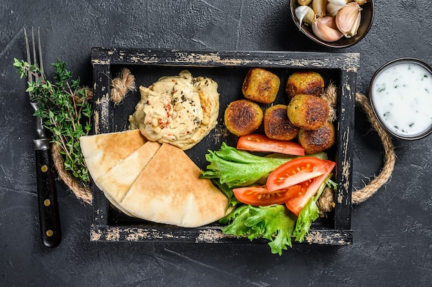 Traditionelle hausgemachte Hummus Kichererbse, Falafel, Fladenbrot und frisches Gemüse. Schwarzer Hintergrund. Ansicht von oben.