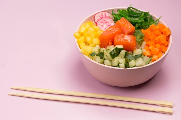 Traditionelle hawaiianische rote Fisch-Poke-Schüssel mit Reis, Tomaten und Meeresalgen Buddha-Schüssel Pinker Hintergrund