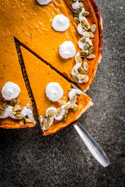 Traditionelle Herbstgerichte. Halloween, Erntedankfest. Geschnittener würziger Kürbiskuchen mit Schlagsahne u. Kürbiskernen auf schwarzer Steintabelle. Ansicht von oben