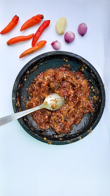 Traditionelle indonesische Chilisauce namens Sambel Trasi Chili mit in Mörser und Pistill zerkleinerten Kräutern isoliert auf weißem Hintergrund