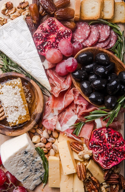 Traditionelle italienische Antipasti-Platte. Verschiedene Käsesorten auf Holzschneidebrett. Brie-Käse, Cheddar-Scheiben, Gogonzola, Walnuss-Trauben, Oliven, Schinken, Rosmarin und ein Glas Rotwein. Draufsicht