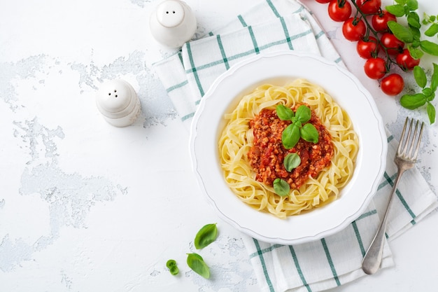 Traditionelle italienische Fettuccine-Nudeln mit Bolognese-Sauce, Basilikum und Parmesan in einem weißen Teller auf hellem Holzhintergrund