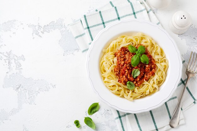 Traditionelle italienische Fettuccine-Nudeln mit Bolognese-Sauce, Basilikum und Parmesankäse in einem weißen Teller auf hellem Holzhintergrund. Ansicht von oben.