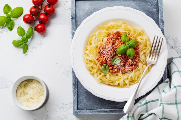 Traditionelle italienische Gericht Fettuccine Pasta mit Bolognese-Sauce, Basilikum und Parmesan in einem weißen Teller auf einer hellen Holzoberfläche