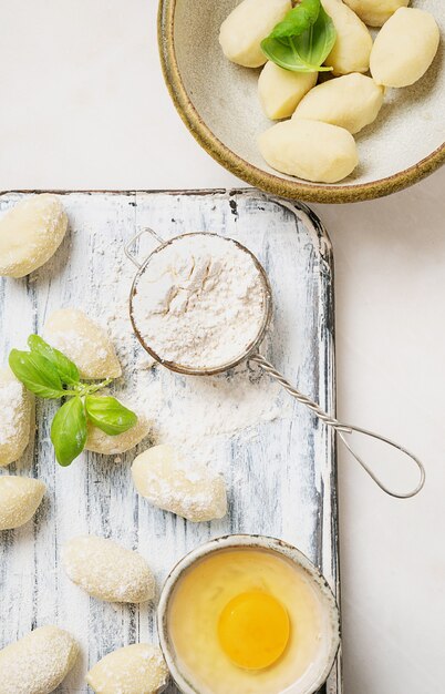 Traditionelle italienische Kartoffel-Gnocci (Nudeln), verziert mit Basilikumblatt, Eiern, Mehl. Konzept für ungekochte Nudeln. Draufsicht. Flache Lage