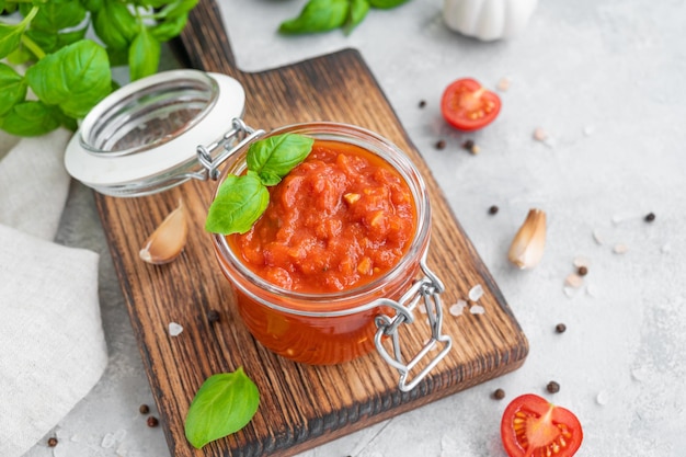 Traditionelle italienische Marinara-Sauce in einem Glas auf Betongrund mit Gewürzen und Zutaten