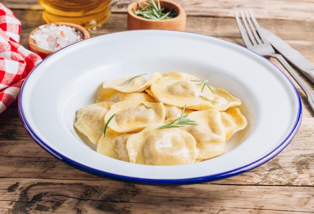 Traditionelle italienische Ravioli mit Rosmarin und gefüllt mit Parmesan auf einem Emailleteller, serviert auf einem rustikalen Holztisch. Italienische Pasta. Selektiver Fokus