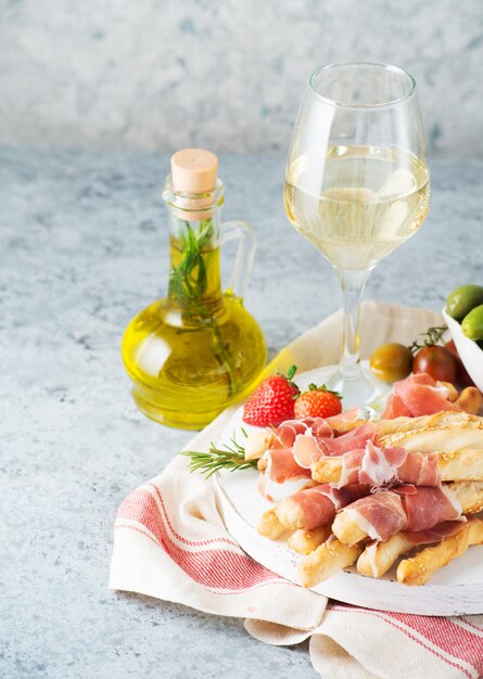 Traditionelle italienische Snacks für Wein, Grissini (Grissini), Tomaten, Prosciutto (Jamon), Erdbeeren und Oliven. Selektiver Fokus, Kopienraum