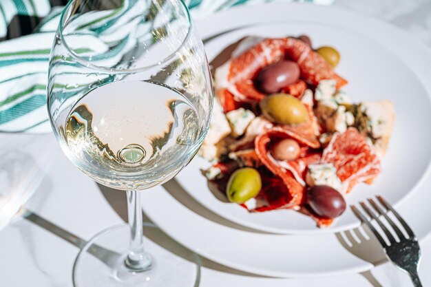 Traditionelle italienische Snacks, Jamon-Oliven und Blauschimmelkäse, gehackter Jamon mit einer Vielzahl von eingelegten Oliven und Stücken von teurem Blauschimmelkäse neben einem Glas kühlem Wein