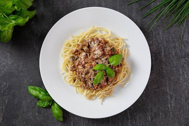 Traditionelle italienische Spaghetti Bolognese mit Fleisch- und Tomatensauce auf einem Teller und mit Parmesan, frischen Tomaten, Basilikum, Gewürzen und Kräutern.