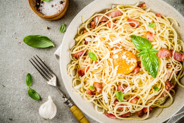 Traditionelle italienische Teigwaren, Spaghettis carbonara mit Speck, sahniger Soße, Parmesankäseparmesankäse, Eigelb und grauer Steintabelle der frischen Basilikumblätter
