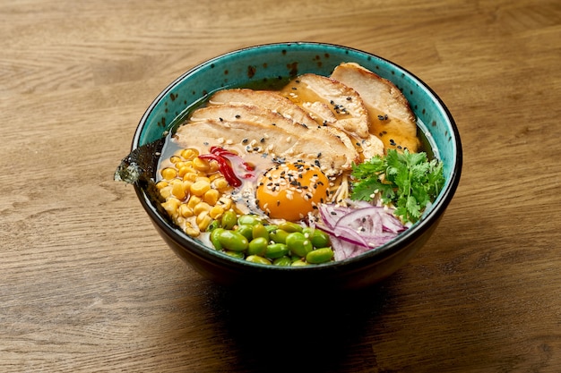 Traditionelle japanische Ramen-Suppe mit Eigelb und Hühnchen, Gemüse in einer Schüssel auf einem Holztisch