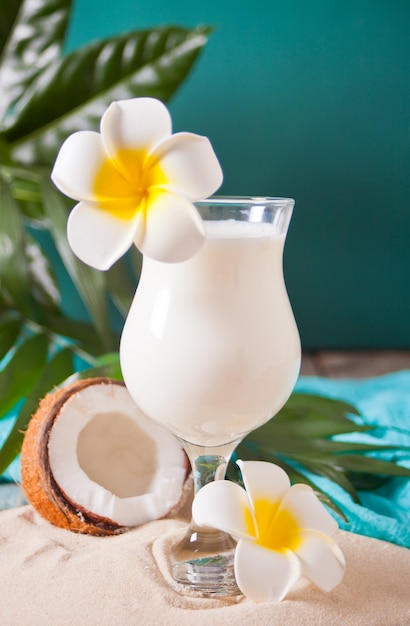 Traditionelle karibische exotische tropische Cocktail trinken Pina Colada in einem Glas mit Plumeria Frangipani Blumen, Palmblatt und Kokosnuss auf dem Hintergrund. Tropisches Strandpicknickkonzept.